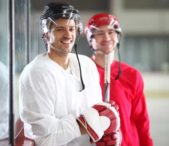Zwei Eishockeyspieler in weißem und rotem Oberteil lächeln in die Kamera