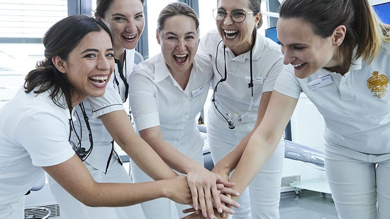Fünf Zahnärztinnen stehen zusammen und haben Handflächen aufeinander gelegt